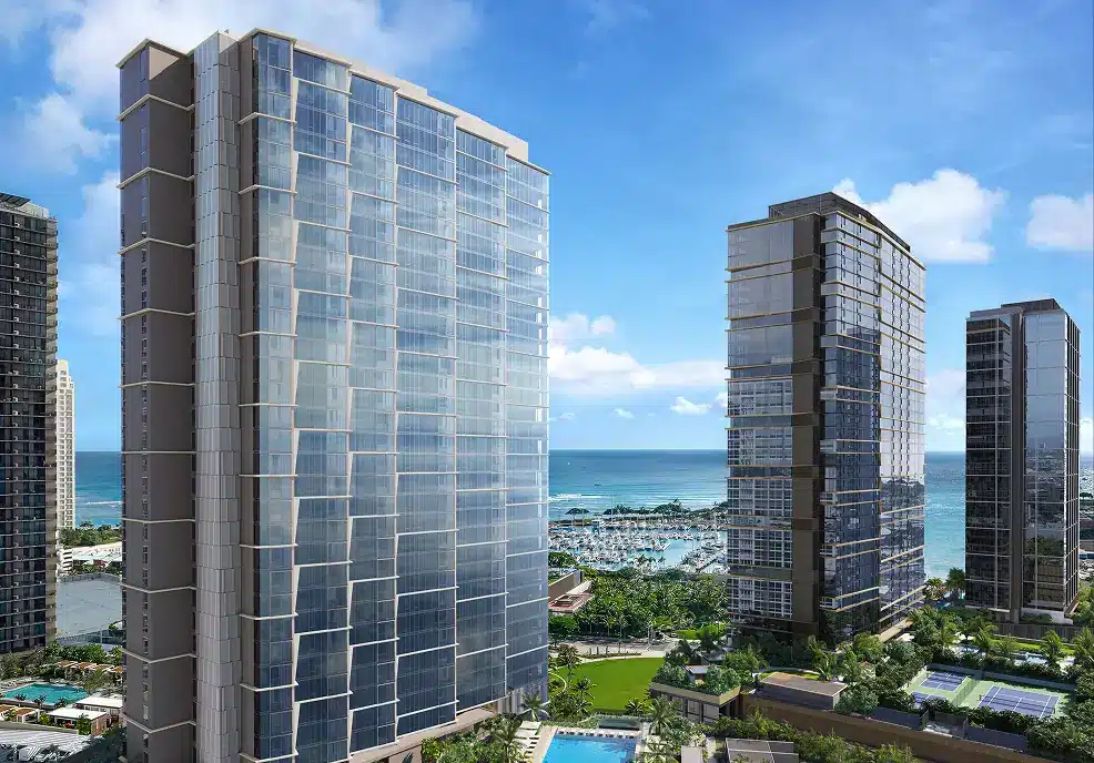 Three modern high-rise buildings with reflective glass windows stand near a marina and the ocean under a blue sky with scattered clouds.