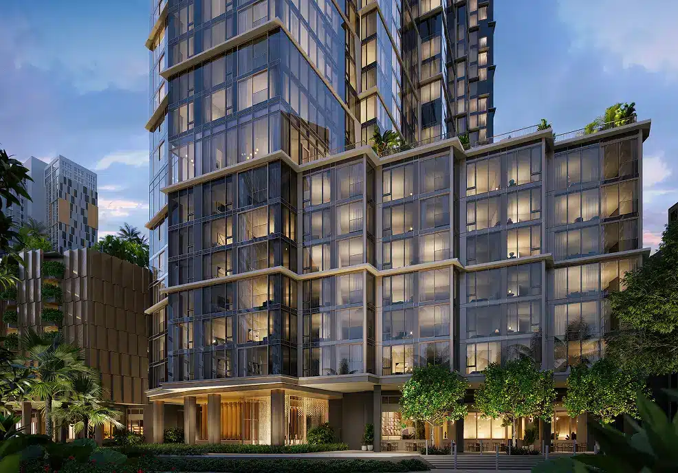 Modern high-rise building with large glass windows, lit from within at dusk; surrounding greenery and cityscape are visible.