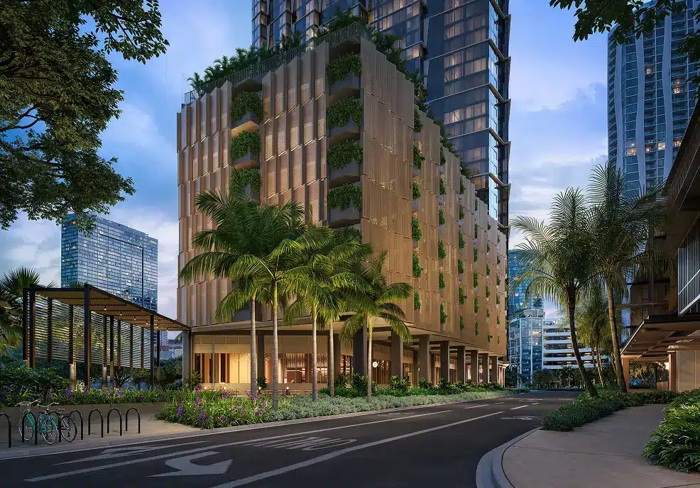 Modern cityscape with a tall building featuring green terraces, palm trees, landscaped gardens, and a curved street in the foreground at dusk.