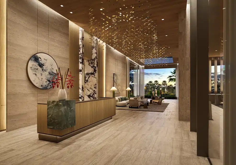 Modern hotel lobby with marble floors, a front desk, abstract wall art, elegant lighting, and large windows offering a view of palm trees outside.