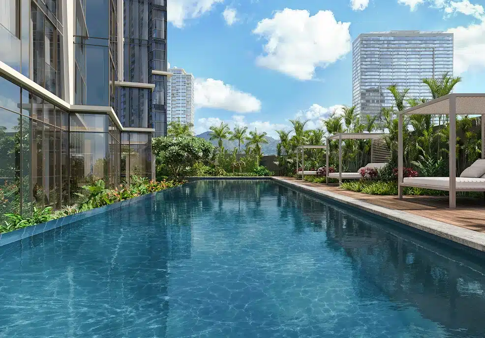 Modern outdoor swimming pool beside a glass building, surrounded by palm trees and cabanas, with high-rise buildings and blue sky in the background.