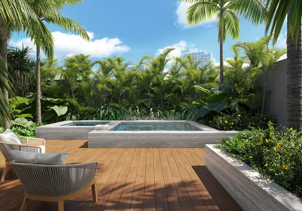 Wood deck patio with two square hot tubs, surrounded by lush palm trees and plants, with two lounge chairs under a sunny blue sky.