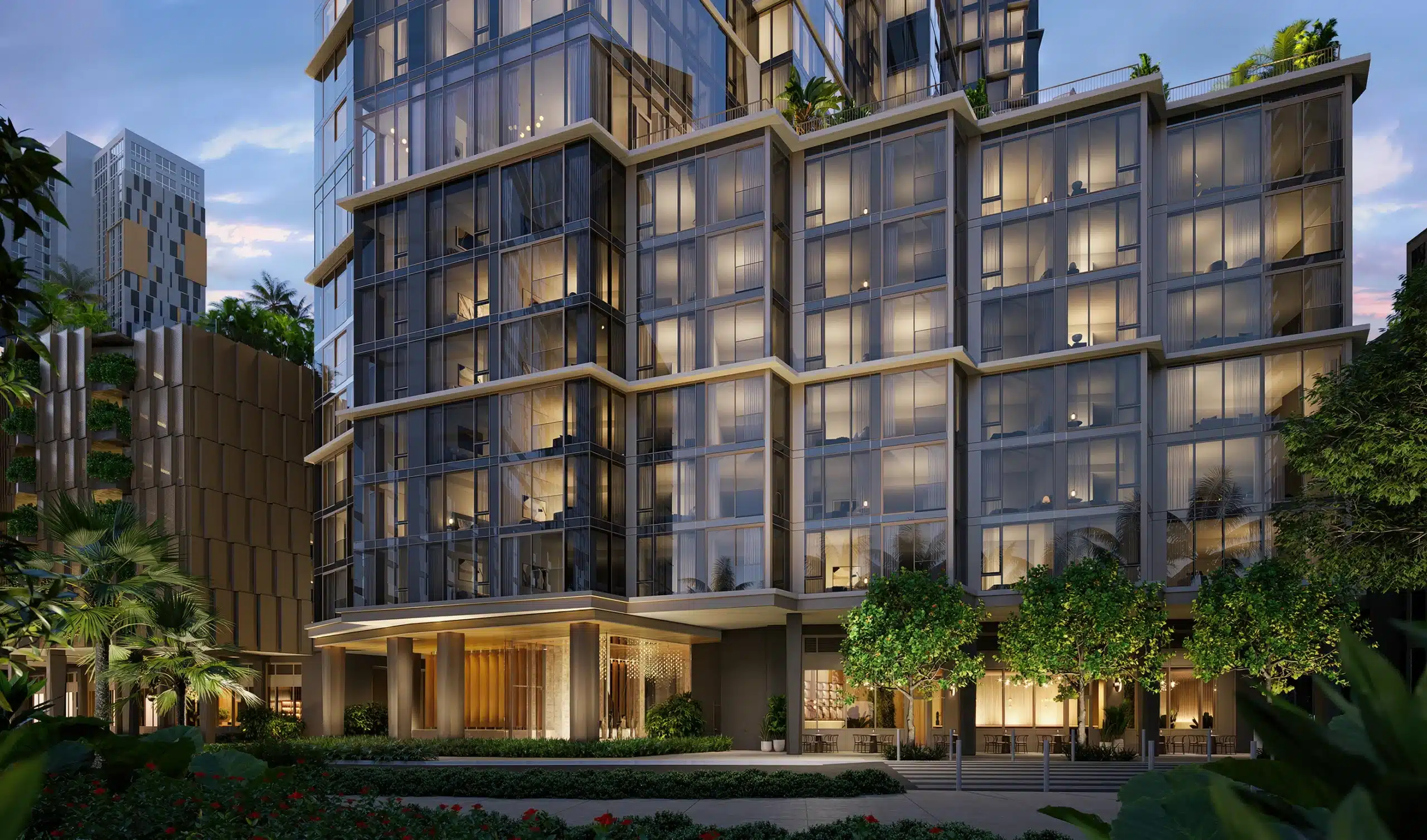 Modern multi-story building with large glass windows, illuminated rooms, and surrounding greenery at dusk.