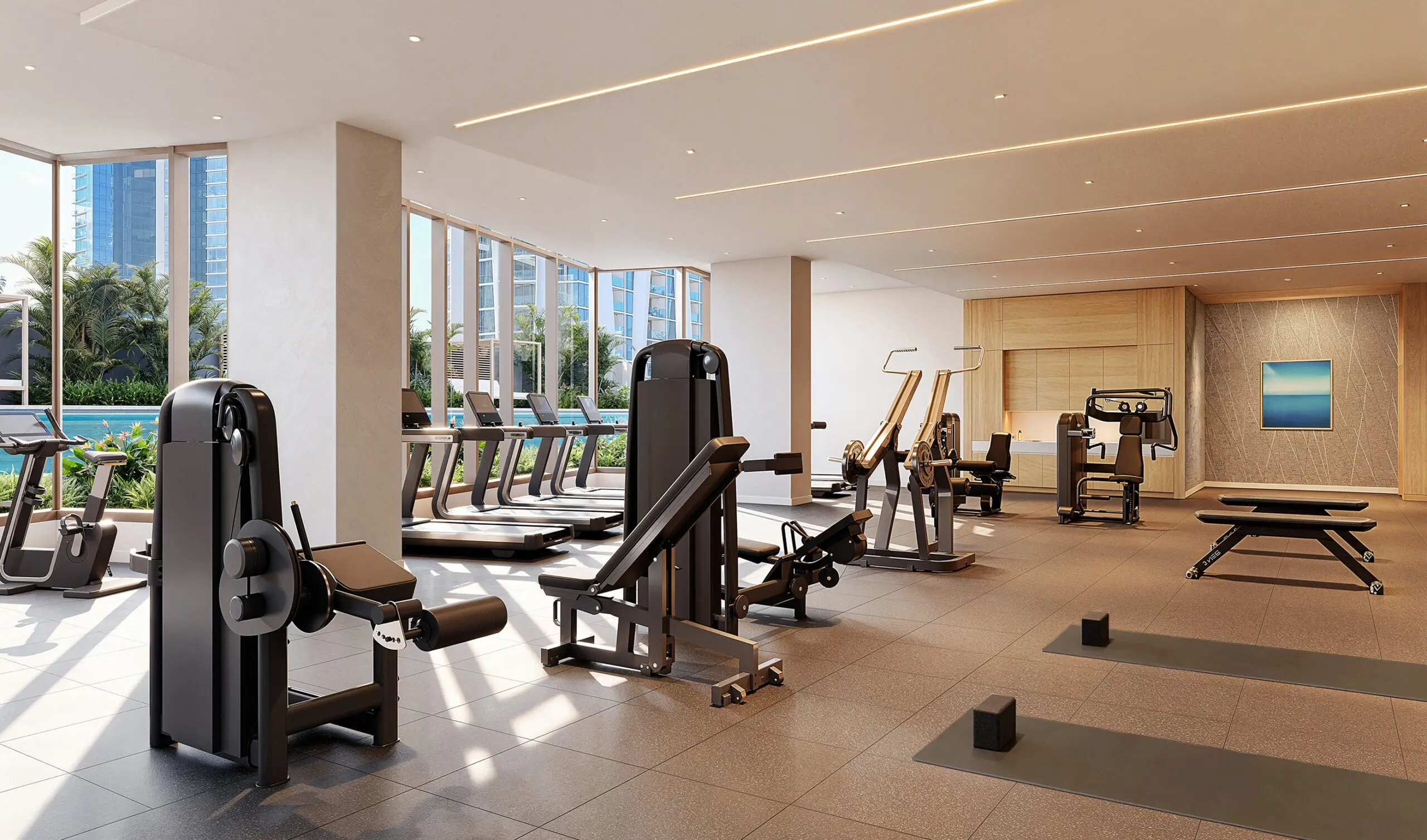 Spacious modern gym with various exercise machines, treadmills by large windows, weight benches, yoga mats, and free weights on a tiled floor. Bright, natural light fills the room.