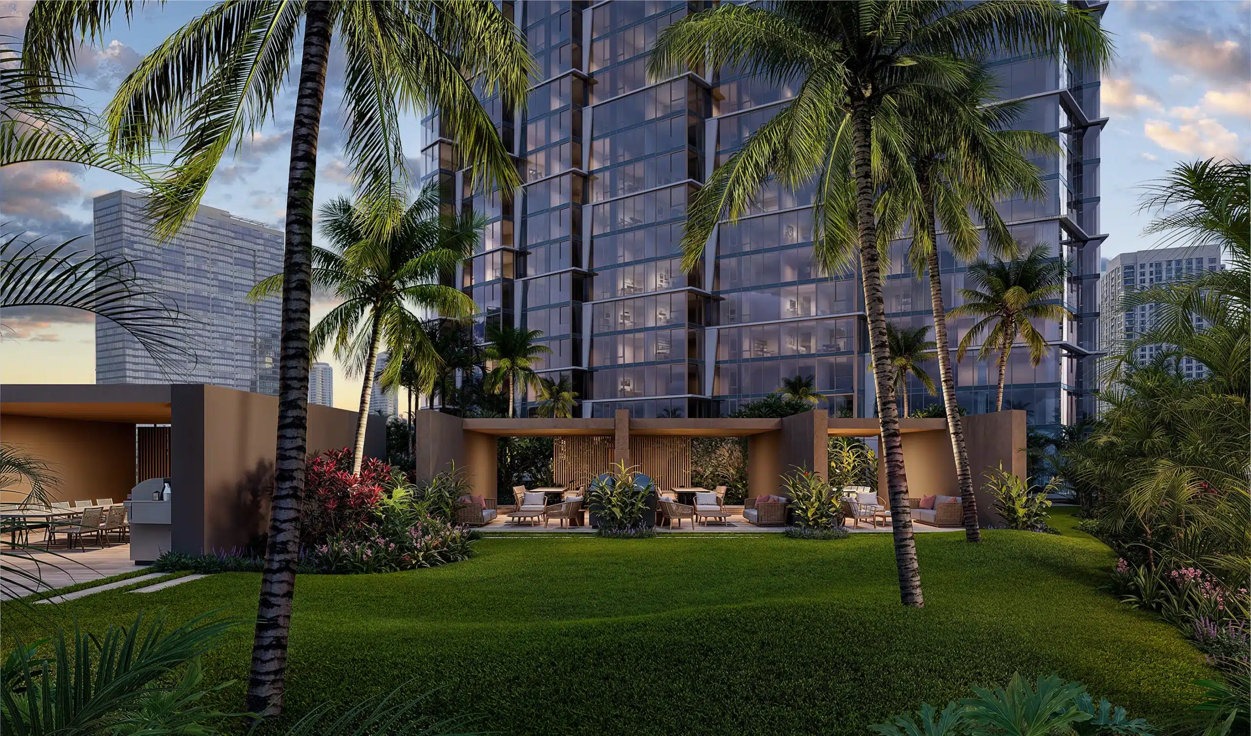 A modern high-rise building with glass windows, surrounded by palm trees, landscaped lawns, and outdoor lounge areas with seating in a tropical urban setting.