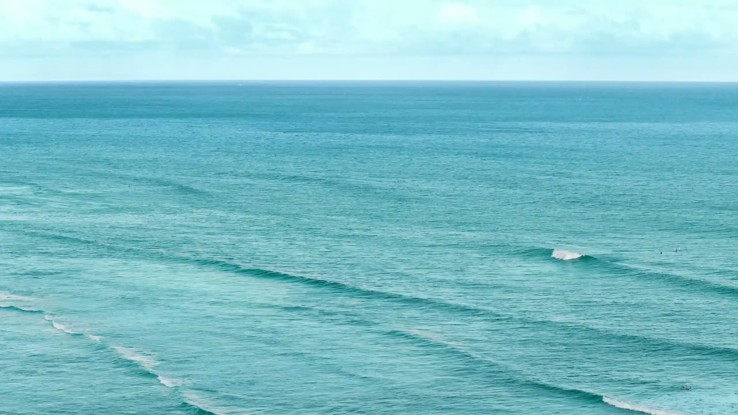 A calm ocean with small waves rolling toward the shore under a cloudy sky.
