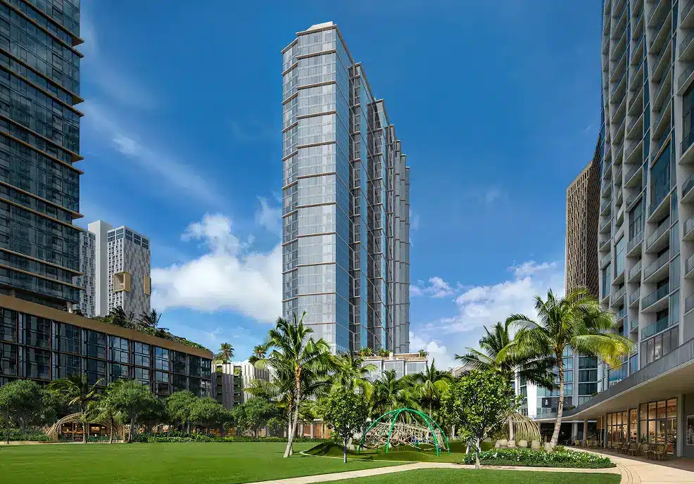 Tall modern glass buildings surround a green park with palm trees, a playground, and clear blue sky in an urban setting.