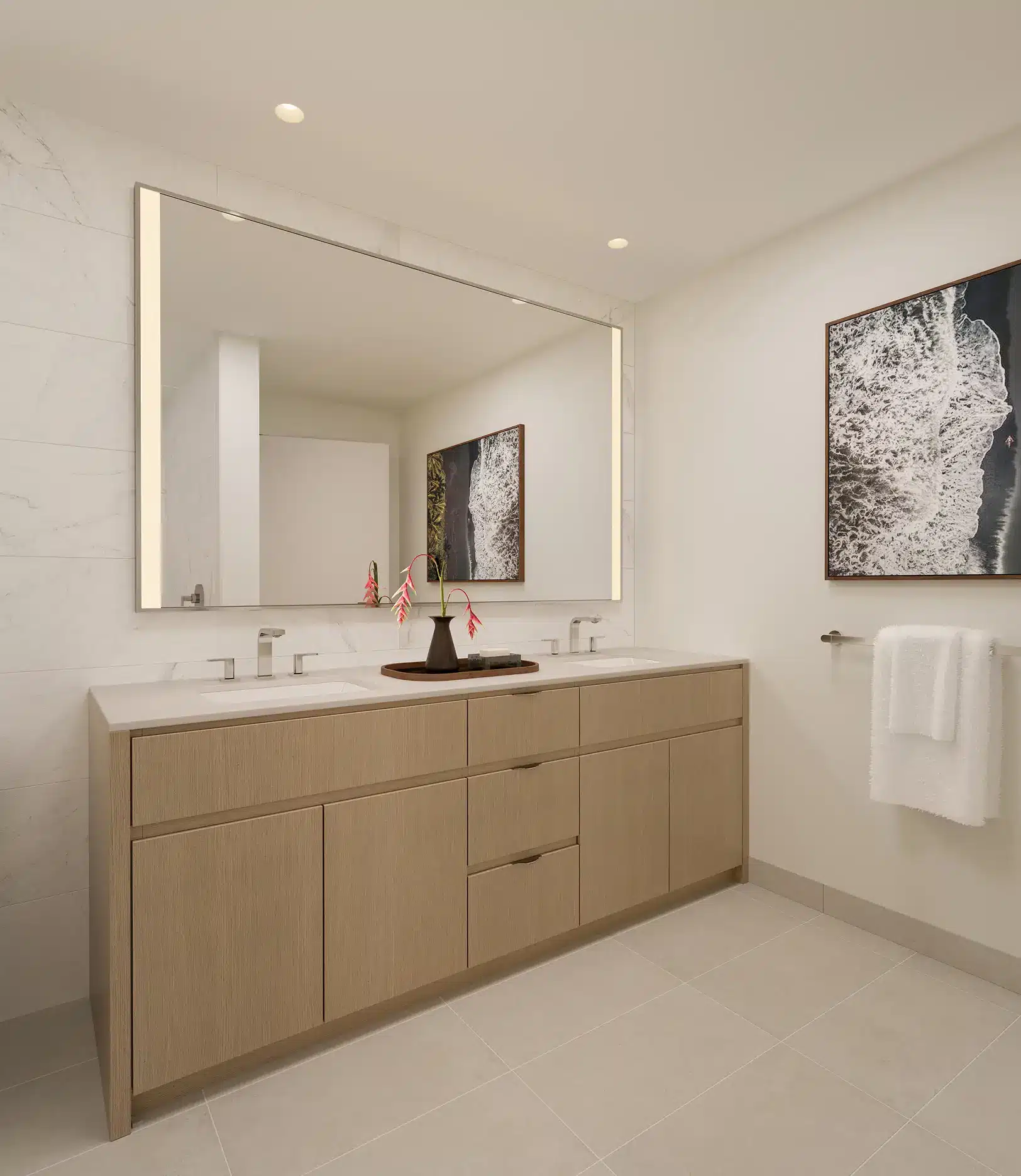Modern bathroom with a large mirror above a double sink vanity, minimalist fixtures, wall art, and a towel hanging on a rack.