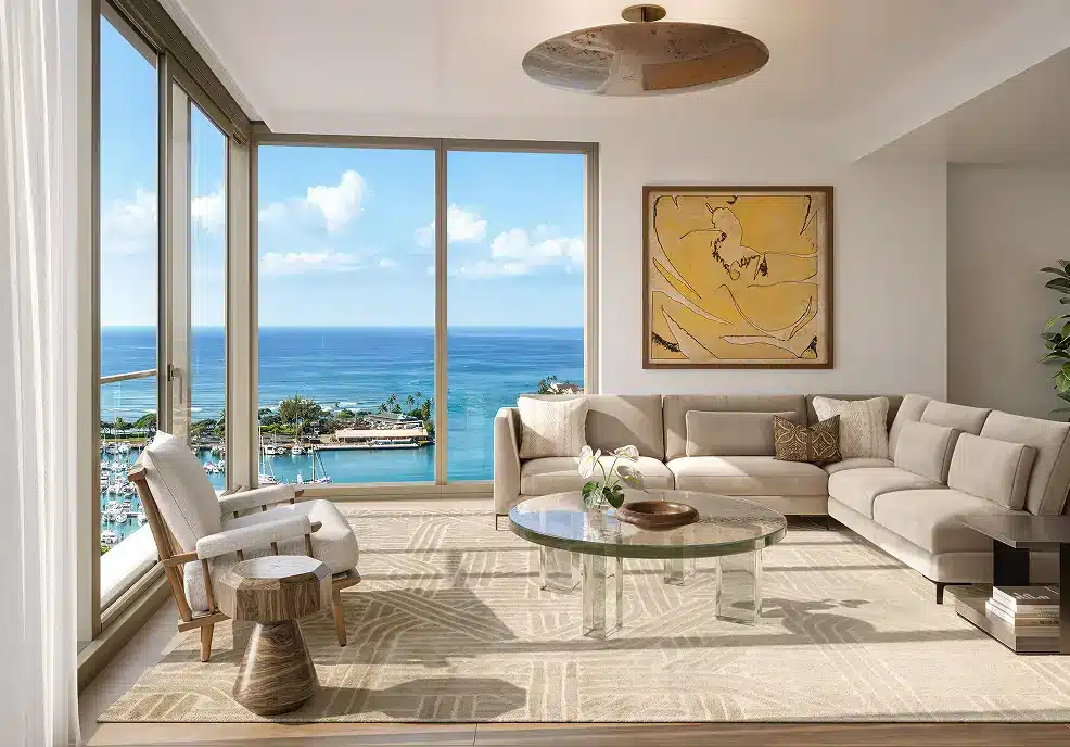 Modern living room with beige sectional sofa, glass coffee table, abstract wall art, and large windows offering an ocean view with a marina and blue sky outside.