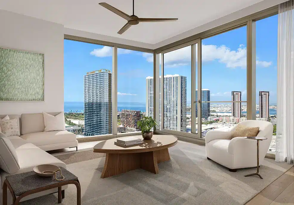 Modern living room with large windows, neutral furniture, a wooden coffee table, a potted plant, and a cityscape view with tall buildings and blue sky outside.