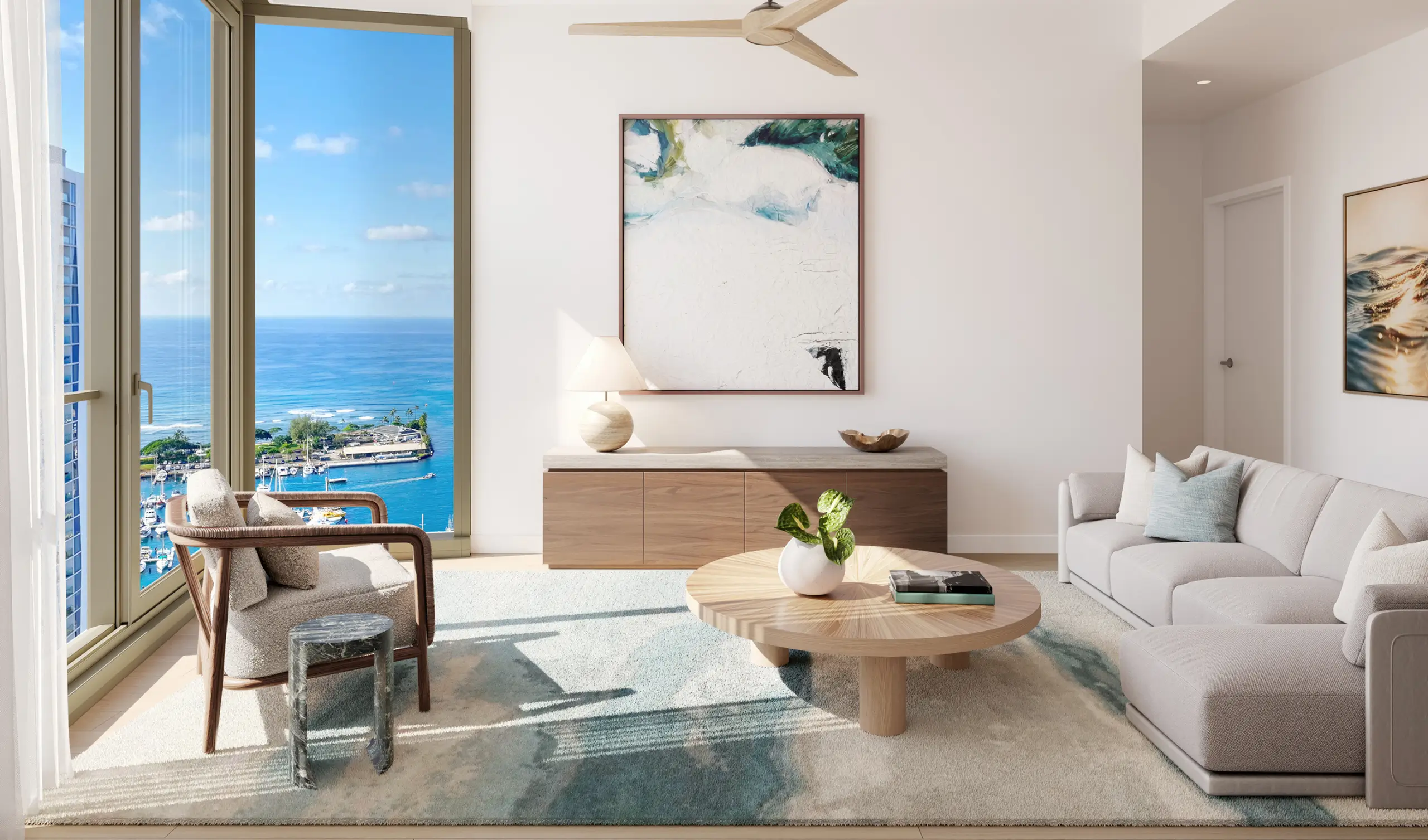 Modern living room with neutral furniture, large window showing an ocean view, abstract art on the walls, and a round coffee table with a plant centerpiece.