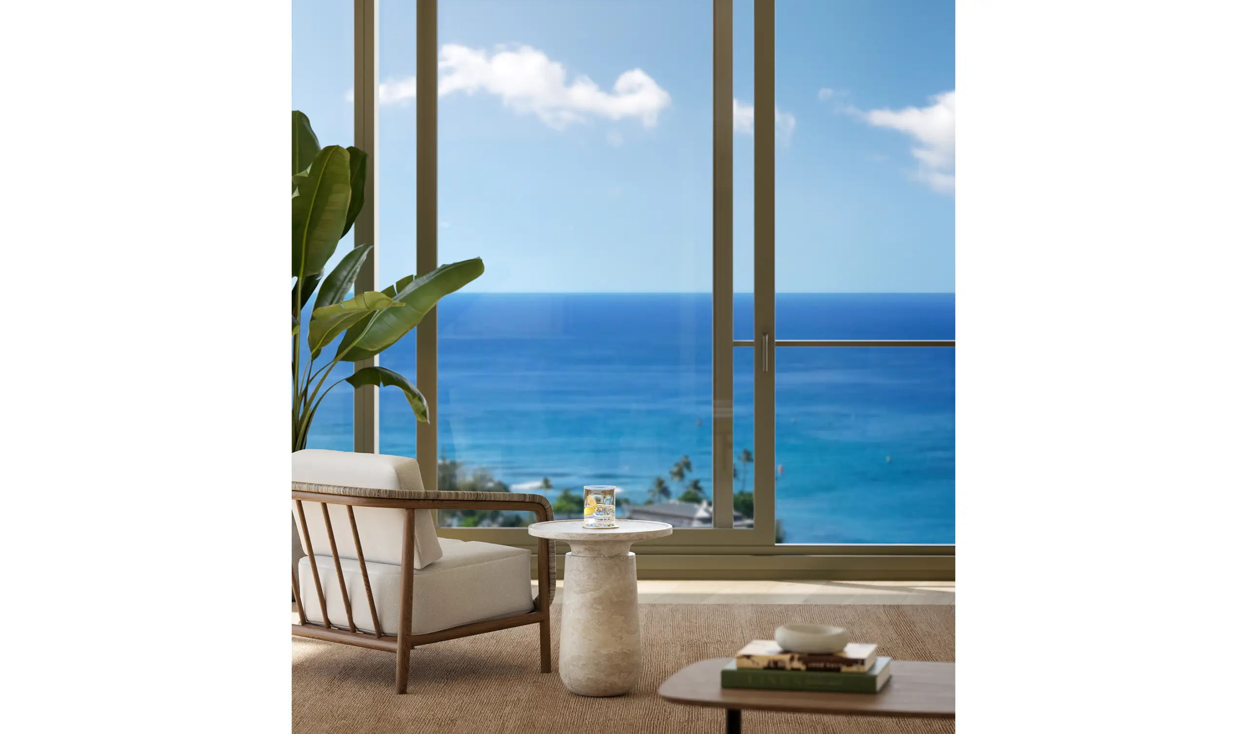 A modern armchair and side table sit by a large window overlooking a blue ocean with a clear sky. A plant and books complete the room’s decor.