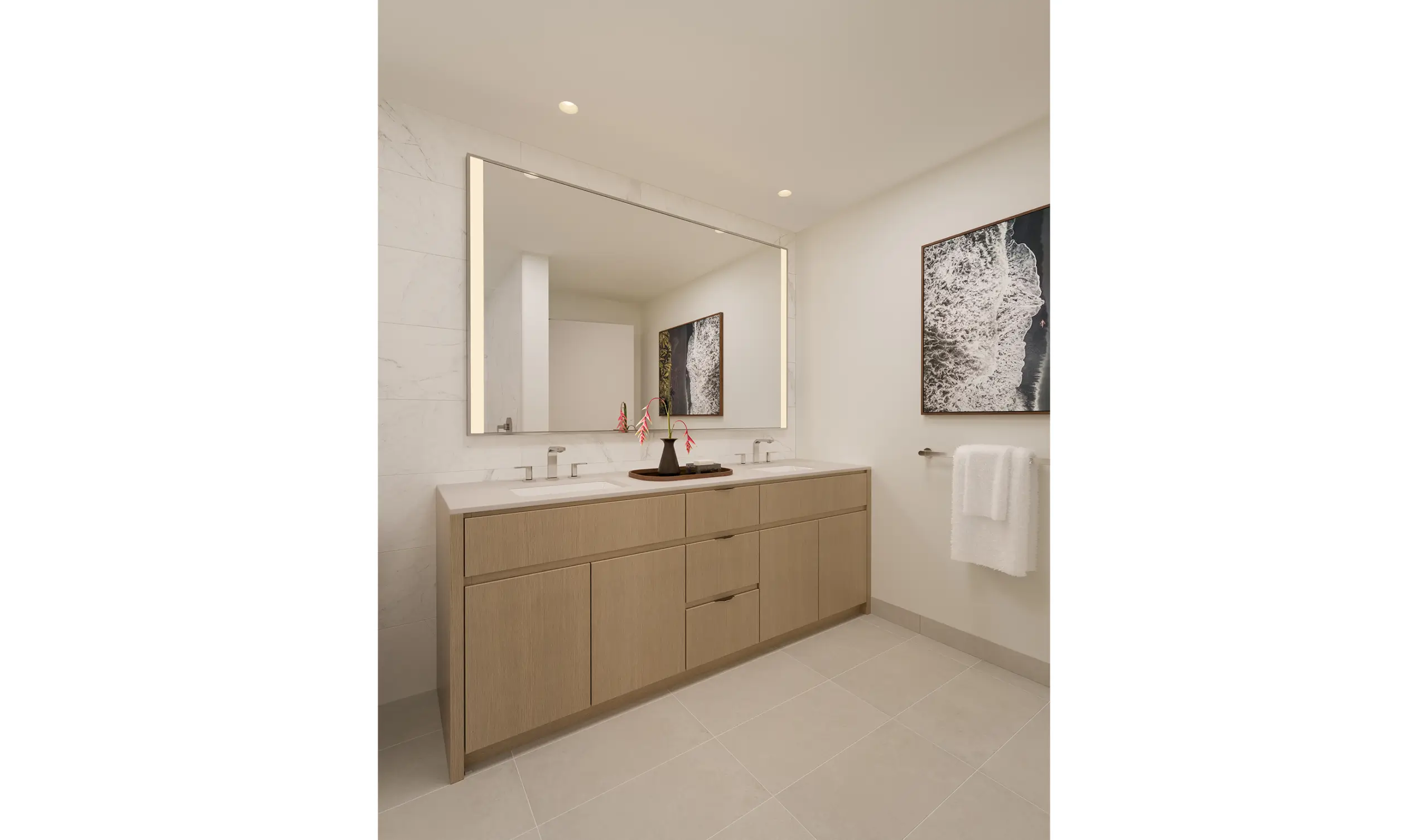 Modern bathroom with a large mirror, double sinks, light wood vanity, white countertop, wall art, and a towel hanging on a rail. Minimalist decor with neutral colors and recessed lighting.